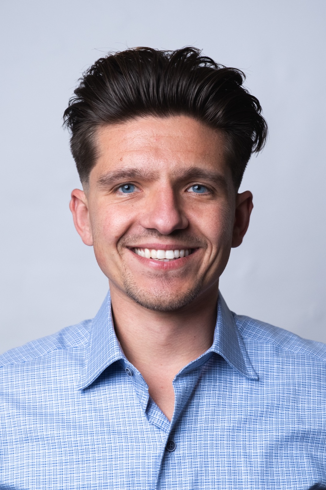 Studio headshot, man in blue shirt smiling